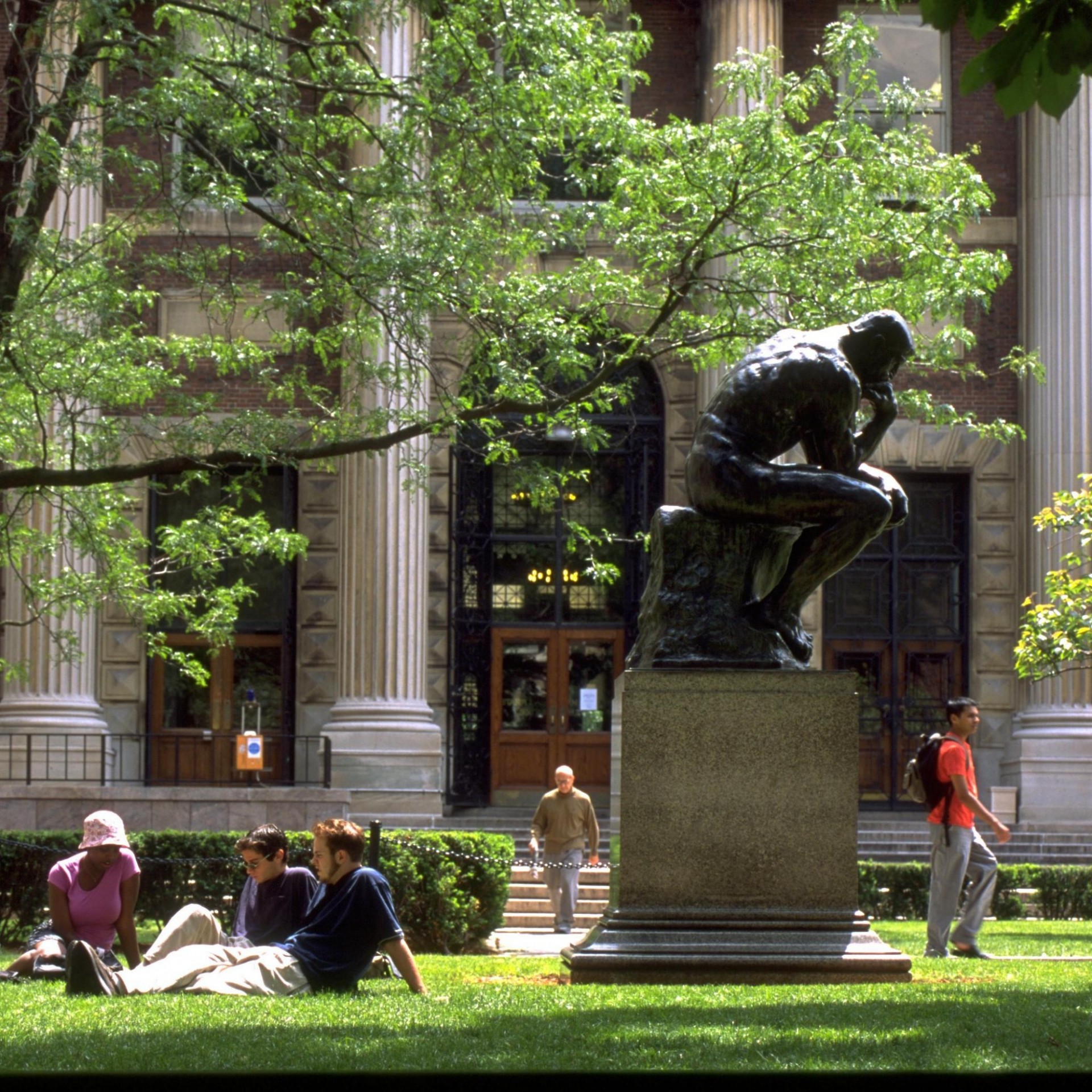 Young adults sitting outside next to statue of a man with his head on his hand.