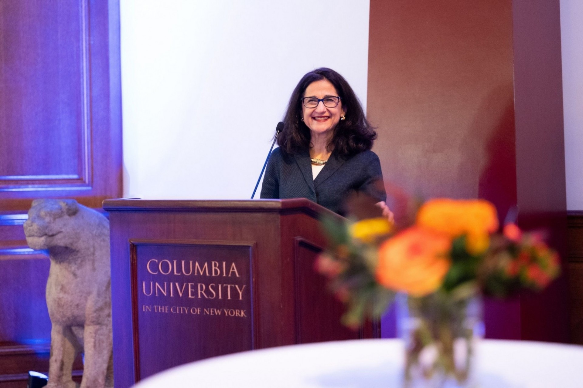 Minouche Shafik, Columbia's president, stands at a podium, smiling, at an evening reception at Columbia University