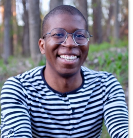 Photo of David Knight sitting in front of trees wearing a striped shirt