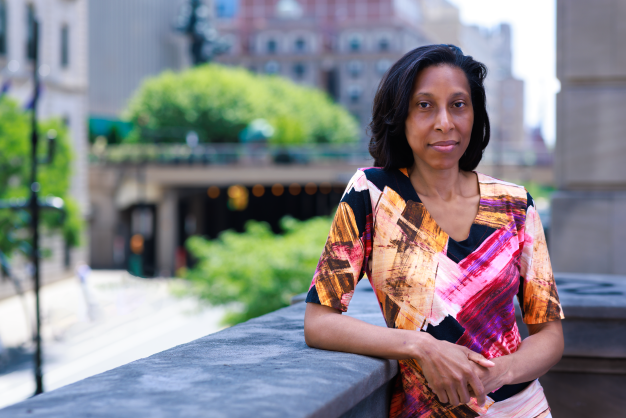 Photo of Ebonya Washington wearing a brown, pink, and black dress, resting on a balcony wall