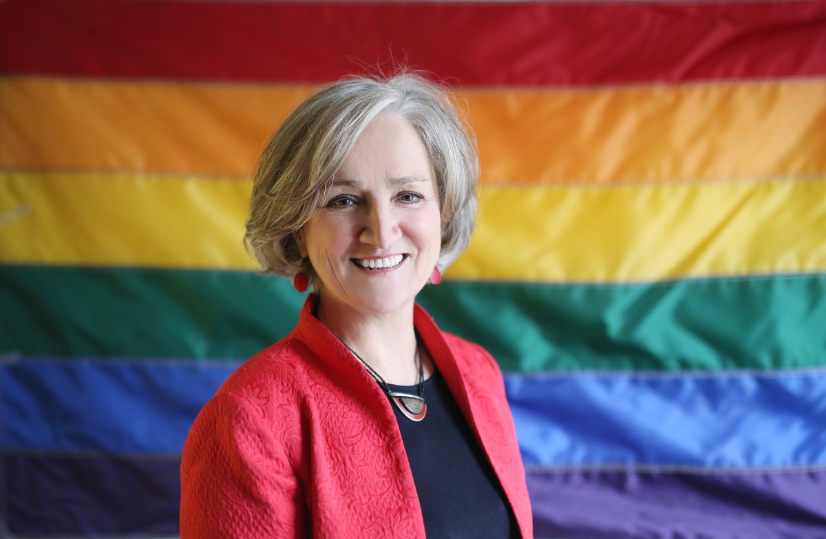 Head shot of Tonda Hughes in front of a rainbow flag