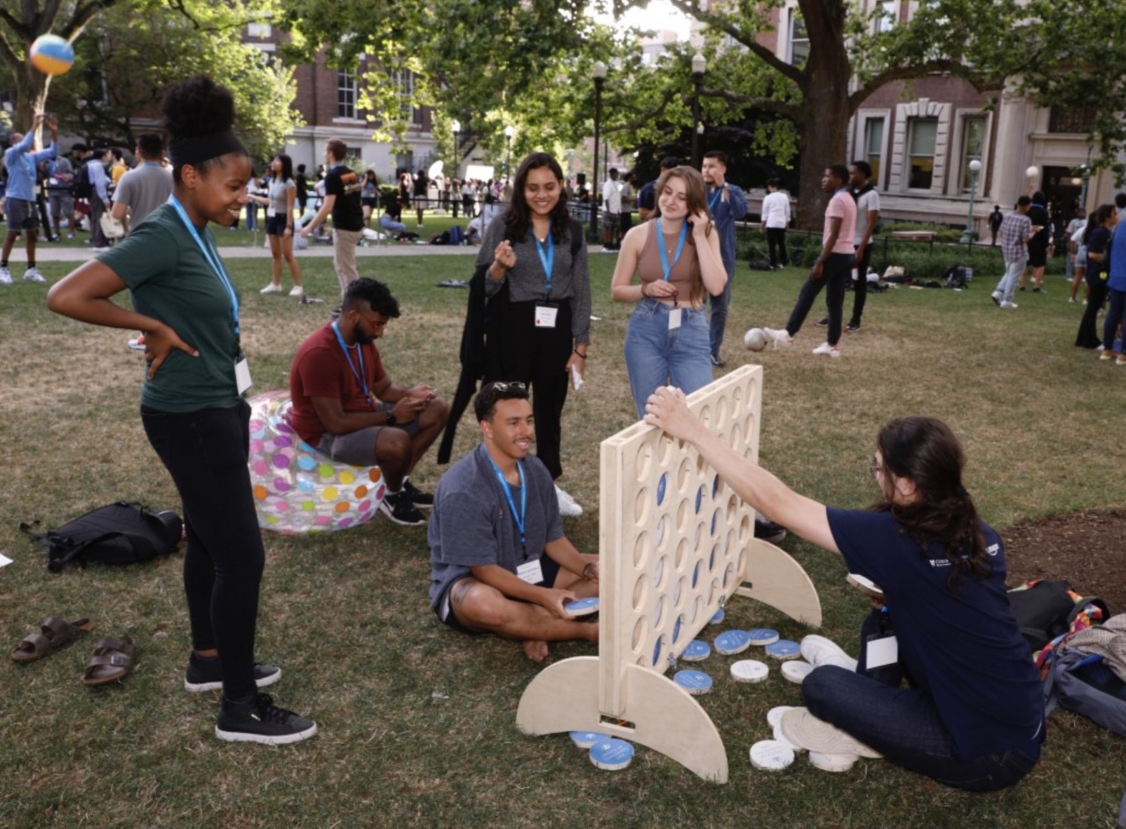 Student in green shirt stands over two students playing a giant Connect Four game on the grass