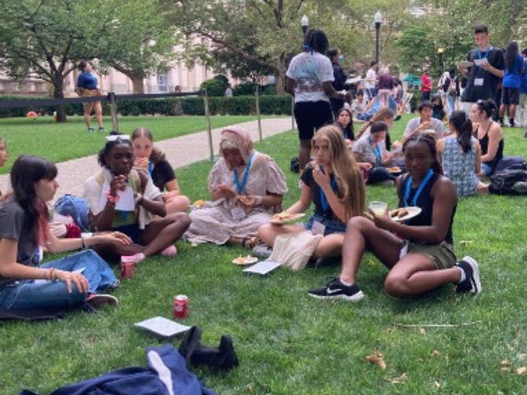 Students attending the CUPP Summer Cookout sit cross-legged on the grass