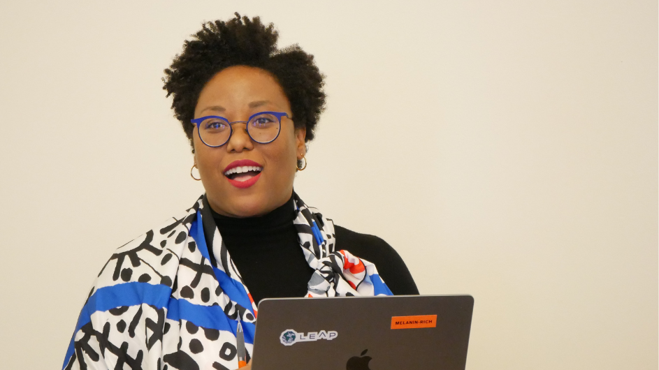 photo of moderator Courtney Cogburn standing and smiling in front of a laptop