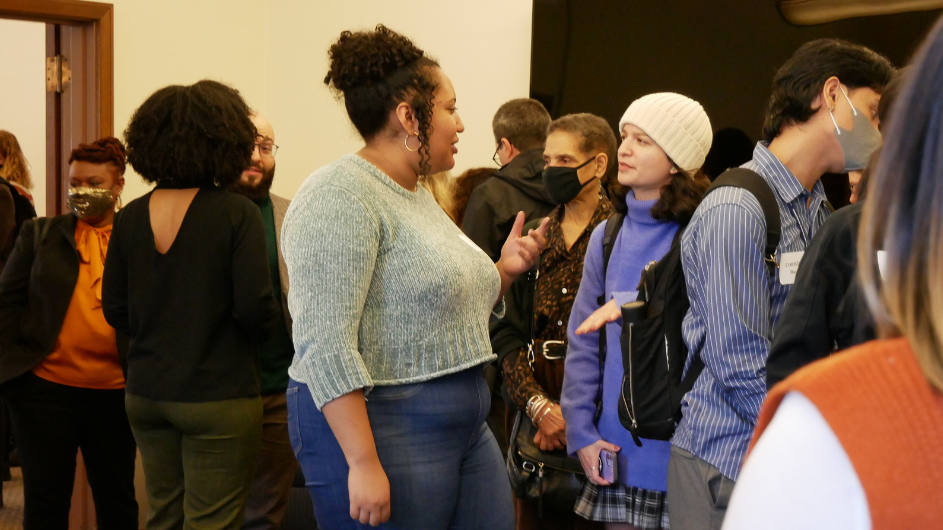 Photo of audience members lined up for food. In the center, two women are talking