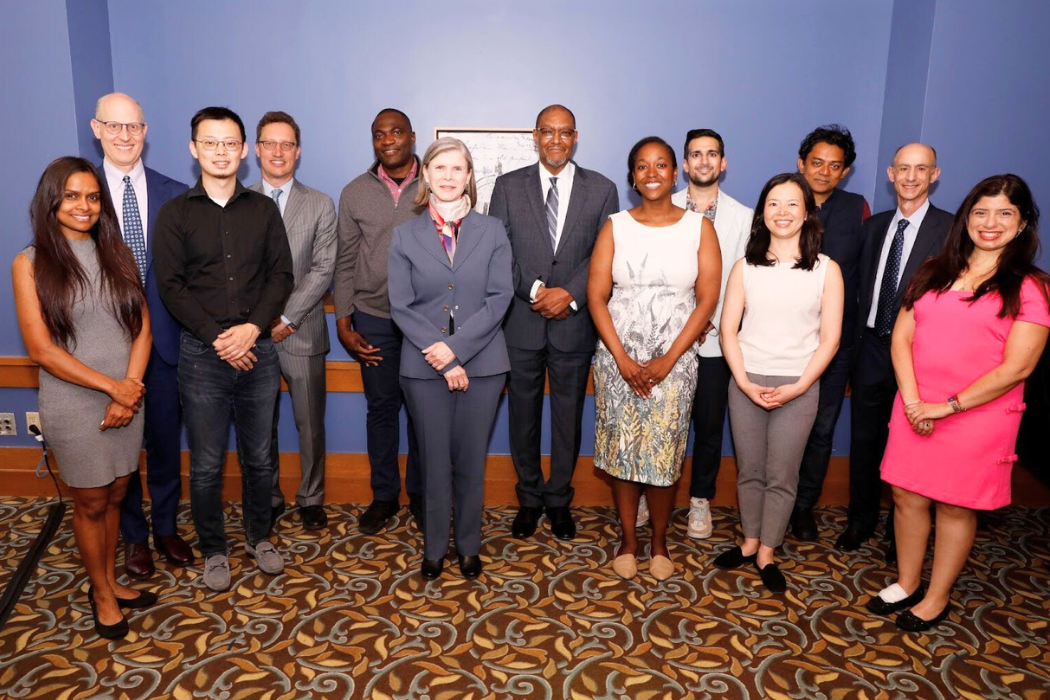 Board members, faculty, and University Administrators smiling in front of blue background