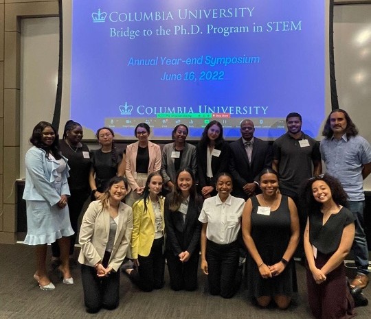 Photo of Bridge Scholars in front of screen with the words "Bridge to the PhD in Stem Annual Year-end Symposium"