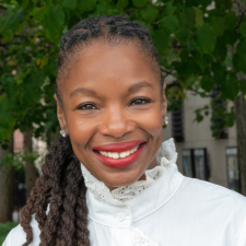 Headshot of Modupe Akinola with long hair and a white ruffled shirt