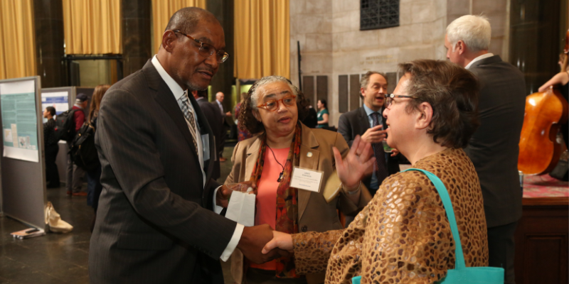 photo of three people, Dennis Mitchell shakes a woman's hand