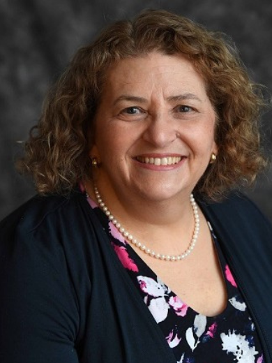 Photo of Amy Rabinowitz wearing a black jacket and floral shirt, with shoulder length curly hair