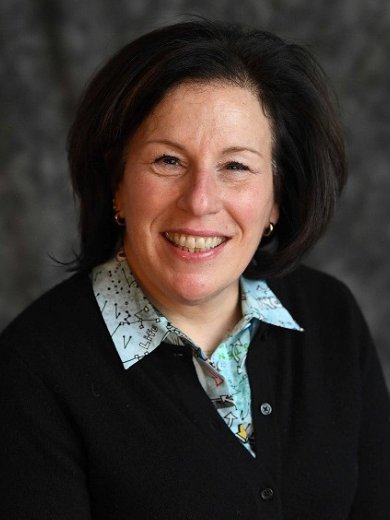 Headshot of Carolyn Sachs Singer wearing a black blazer and light blue shirt smiling at the camera