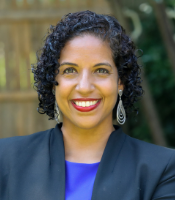 Photo of Adina Brooks with curly brown hair and a blue shirt and navy jacket