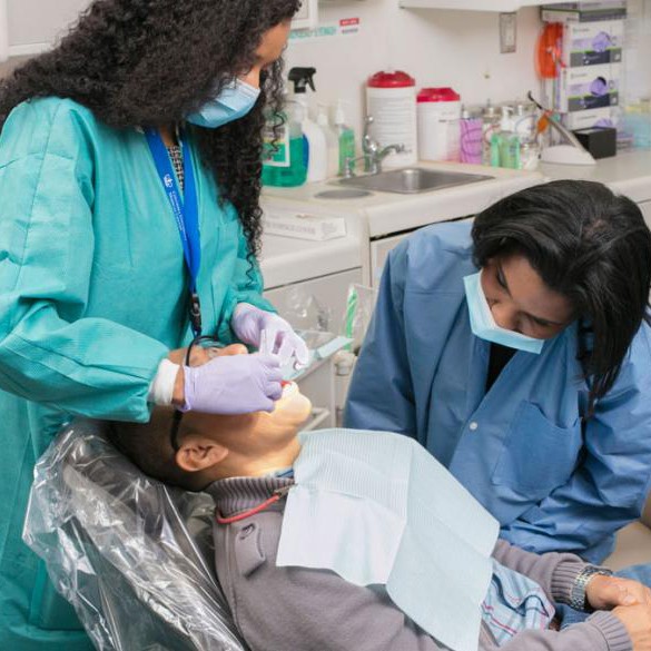 Female dentist examines the mouth of a patient while a student watches.