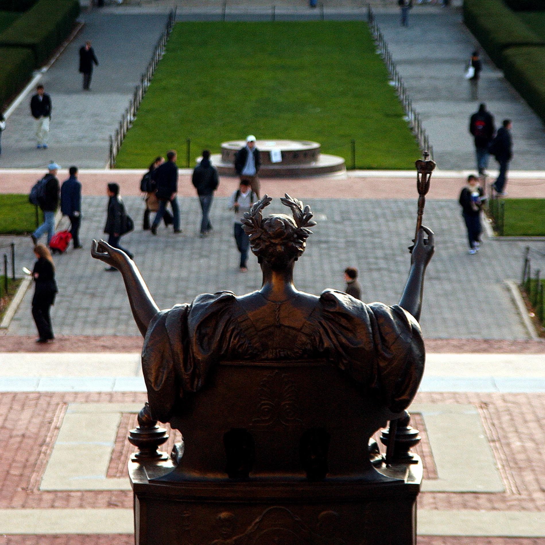 Statue of woman with outstretched arms behind plaza with many people walking by