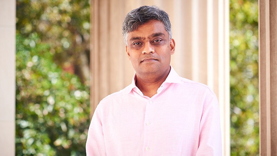Headshot of Garud Iyengar. He is wearing a pink shirt, standing outdoors in front of a building column on a sunny day.