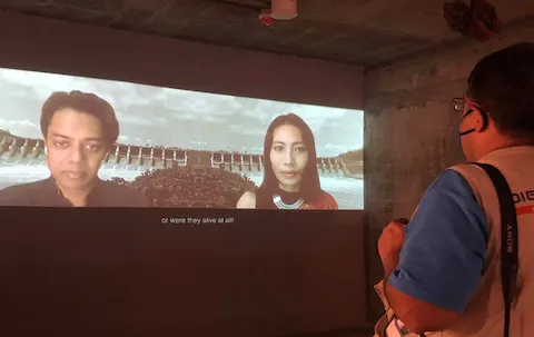 Photo of video installation with faces of Naeem Mohaiemen and Samari Chakma on the screen