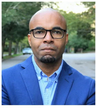Head shot of Mario Small wearing a blue shirt and jacket and glasses.
