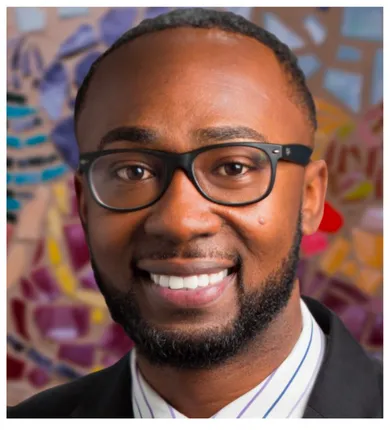 Head shot of Charles Lea with short beard and glasses. He is standing in front of a mosaic on the wall behind him