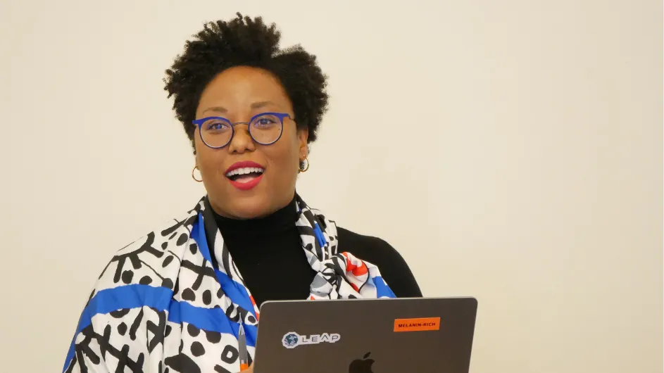 photo of moderator Courtney Cogburn standing and smiling in front of a laptop