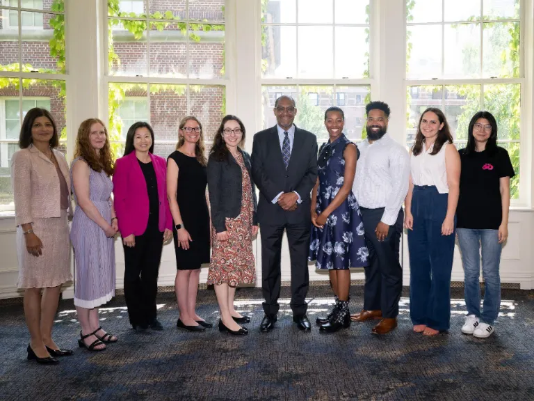 10 smiling people stand in front of a window 