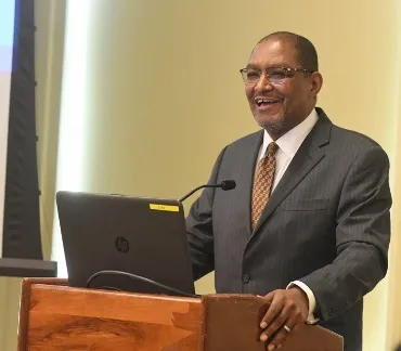 Photo of Dennis Mitchell standing at a podium smiling