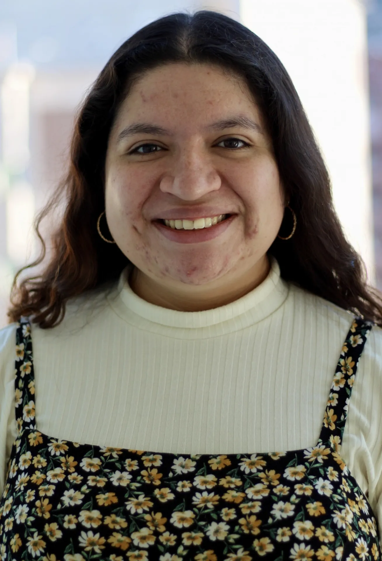 Mariah Ramos, a young white female, with long brown hair, dressed in a black dress with yellow flower pattern and white shirt underneath
