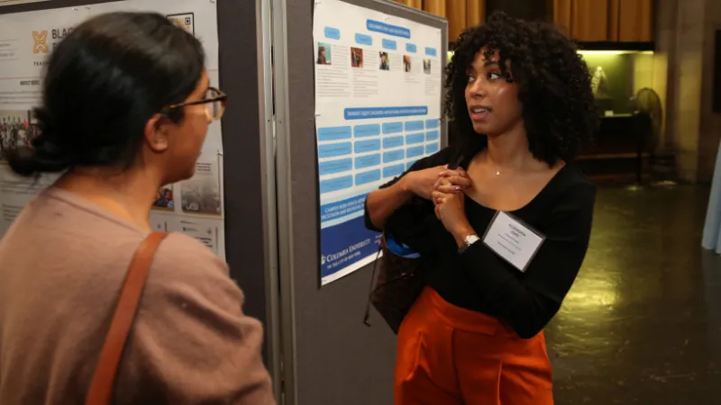 Photo of two women speaking in front of posters.