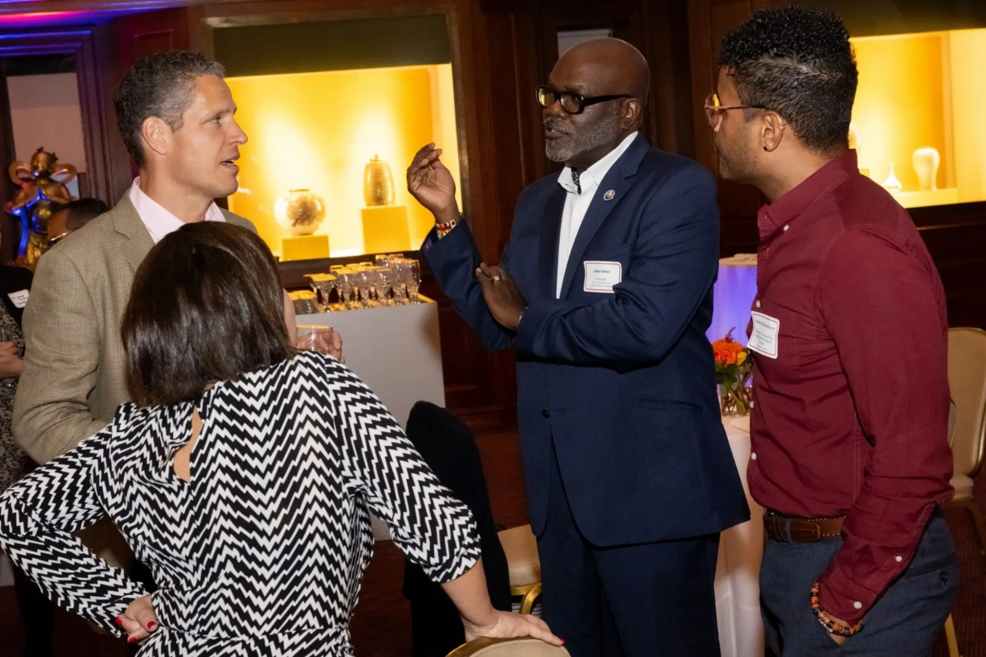 A diverse group of three men and a woman in engaged conversation at a cocktail reception.