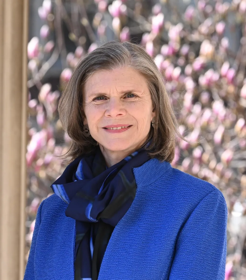 Portrait of Angela Olinto in a blue jacket with a scarf, standing outside. 