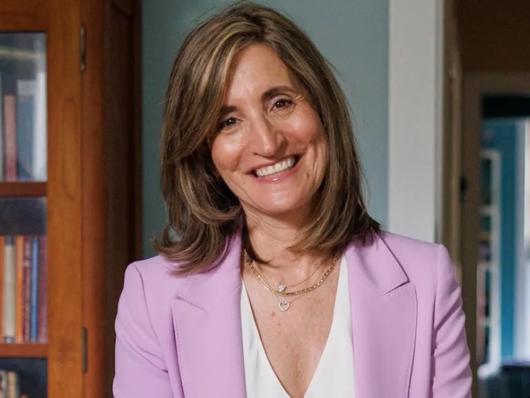 Julie Kornfeld, smiling, wears a pink blazer and white shirt