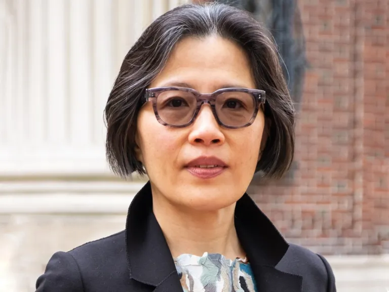 Weiping Wu wears glasses and stands in front of brick building in black blazer and colorful shirt.
